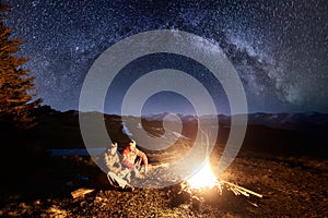 Two male hikers have a rest in the camping at night under beautiful night sky full of stars and milky way. Long exposure