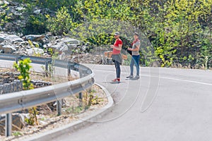 Two male longboarders carrying their longboards in their hands while climbing uphill and preparing for a downhill slide. Wearing