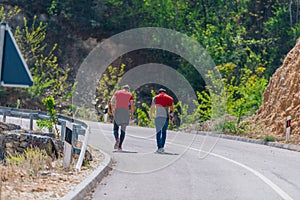 Two male longboarders carrying their longboards in their hands while climbing uphill and preparing for a downhill slide. Wearing
