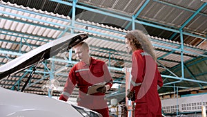 Two male mechanics working as mechanics in garage together, two mechanics stand talk together in front bonnet that opens perform