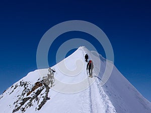 Two male mountain climbers on an exposed snow summit ridge in the Swiss Alps