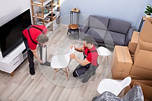 Two Male Mover Wrapping Furniture For Moving