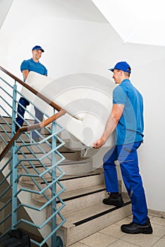 Two Male Movers Carrying Sofa On Staircase