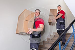 Two Male Movers Walking Downward With Boxes On Staircase