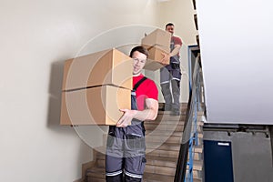 Two Male Movers Walking Downward With Boxes On Staircase photo