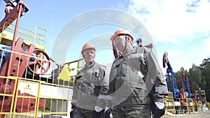 Two male oil workers walking and talking near oil pump jacks. Oil engineers overseeing drilling rig of crude oil