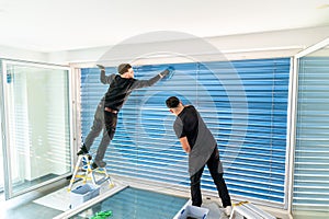 Two male professional cleaners cleaning blue blinds on a large window front with micro fiber cloths
