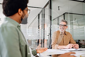 Two male professional colleagues are engaged in a friendly discussion at the office