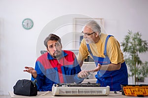 Two male repairmen repairing air-conditioner