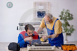 Two male repairmen repairing air-conditioner