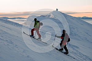 two male skiers climb up to the top of a snowy mountain slope