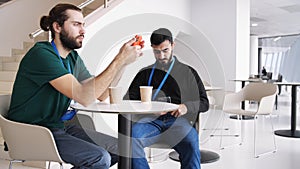 Two male with smartphones inside building with white interior. Media. Handsome young businessmen sitting at the table