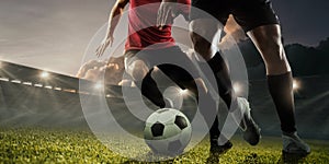 Two male soccer, football players dribbling ball at the stadium during sport match on dark sky background.