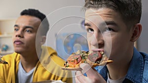 Two male teenagers watching tv and eating pizza, fatty cheap snacks, fast food
