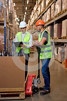 two male warehouse workers with hand pallet jack lift stand discussing, temwork