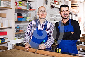 Two male woodworkers posing at workplace in workshop and smiling