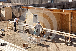 Two male workers prepare wooden planks for construction on a sawmill. Construction carpentry. Fasteners and installation of roof