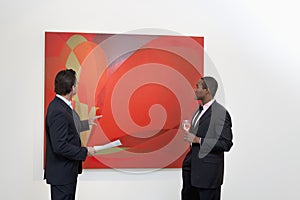 Two males talking over painting in art gallery