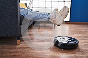 Two man couple using laptop and vacuum cleaner robot sitting on sofa at home