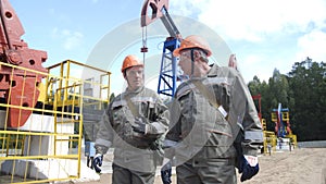 Two man oil workers walking and talking near oil pump jacks. Oil engineers overseeing site of crude oil production