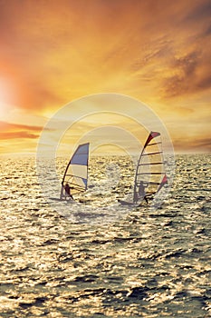 two man playing wind surf over rushing sea against beautiful sunset lighting