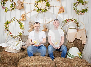 Two man with rabbit ears sitting on the haystack and holding Easter eggs