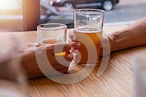 Two man`s hands holding beer glasses or clinking in the pub