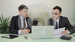 Two managers working, sitting at table with laptop in modern office