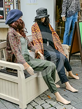 Two mannequins display dummy sitting on a white bench
