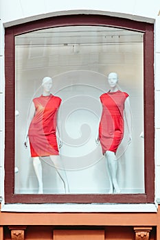 Two mannequins of a female figure in red dresses in a window.