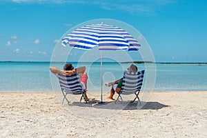 Two mans is sitting in chairs under parasol on a tropical beach. Summer vacation concept