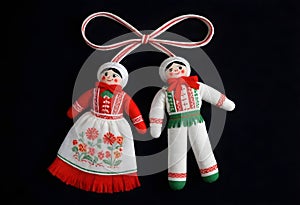 two martenitsa dolls in traditional clothing are hanging from a ribbon on black background