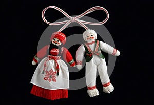 two martenitsa dolls in traditional costumes are hanging from a ribbon