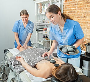 Two massage therapists doing full body stone massage to young woman