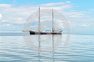 A two-masted ship is reflected on the surface of the water at sea