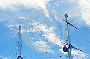 Two masts of a yacht with rigging seen against a blue sky with white clouds.