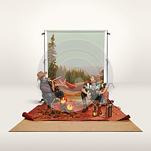 Two mates, men recreating camping activity over grey background with nature wallpaper. Good time. Imagination