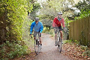 Two Mature Male Cyclists Riding Bikes Along Path