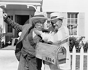 Two mature men fighting near a mail box in front of a house