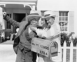 Two mature men fighting near a mail box in front of a house