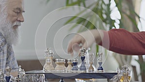 Two mature senior friends playing chess sitting at home. Caucasian old men neighbors playing chess joyfully indoors