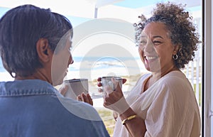 Two Mature Women Friends In Beachfront House Overlooking Ocean For Summer Vacation With Hot Drinks photo