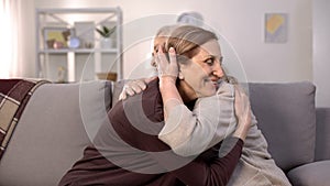 Two mature women hugging sitting on sofa in living room, sisters love, family