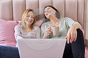 Two mature women looking at laptop sitting at home in bed