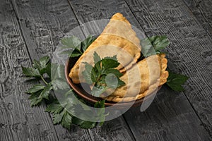 Two meat pies in a clay bowl and parsley leaves on a wooden background