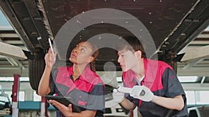 Two mechanic worker partners check car undercarriage at the service garage.