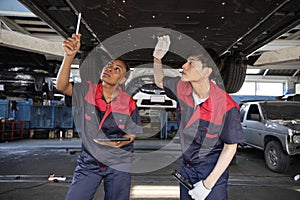 Two mechanic worker partners check car undercarriage at the service garage.