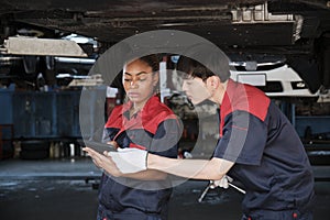Two mechanic worker partners check car undercarriage at the service garage.