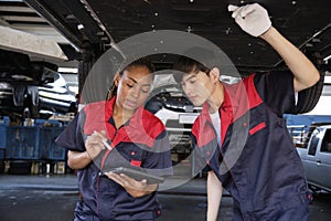 Two mechanic worker partners check car undercarriage at the service garage.