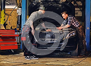 Two mechanics fixing car`s engine in a garage.